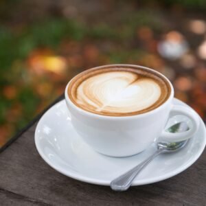A beautifully crafted latte with heart art sits on a wooden table outdoors.