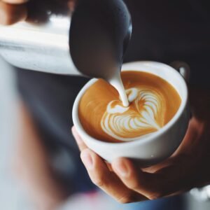 Close-up of barista pouring milk to create stunning latte art in a coffee shop setting.