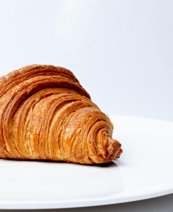 Crisp and flaky golden croissant on a plain white plate, freshly baked to perfection.