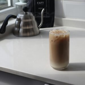 High angle glass of delicious iced latte and metal coffee kettle placed on white table in kitchen