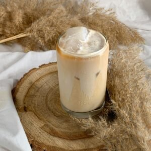 A refreshing iced cappuccino on a rustic wooden tray surrounded by dried pampas grass.