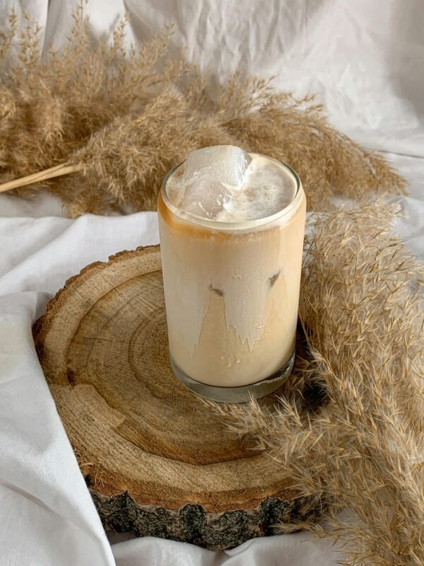 A refreshing iced cappuccino on a rustic wooden tray surrounded by dried pampas grass.